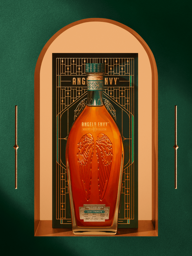 Angel’s Envy 2026 Cask Strength Bourbon bottle displayed in front of the limited-edition presentation box,  framed by an arched niche within the Cask Archive room and set in the Cask Archives room.